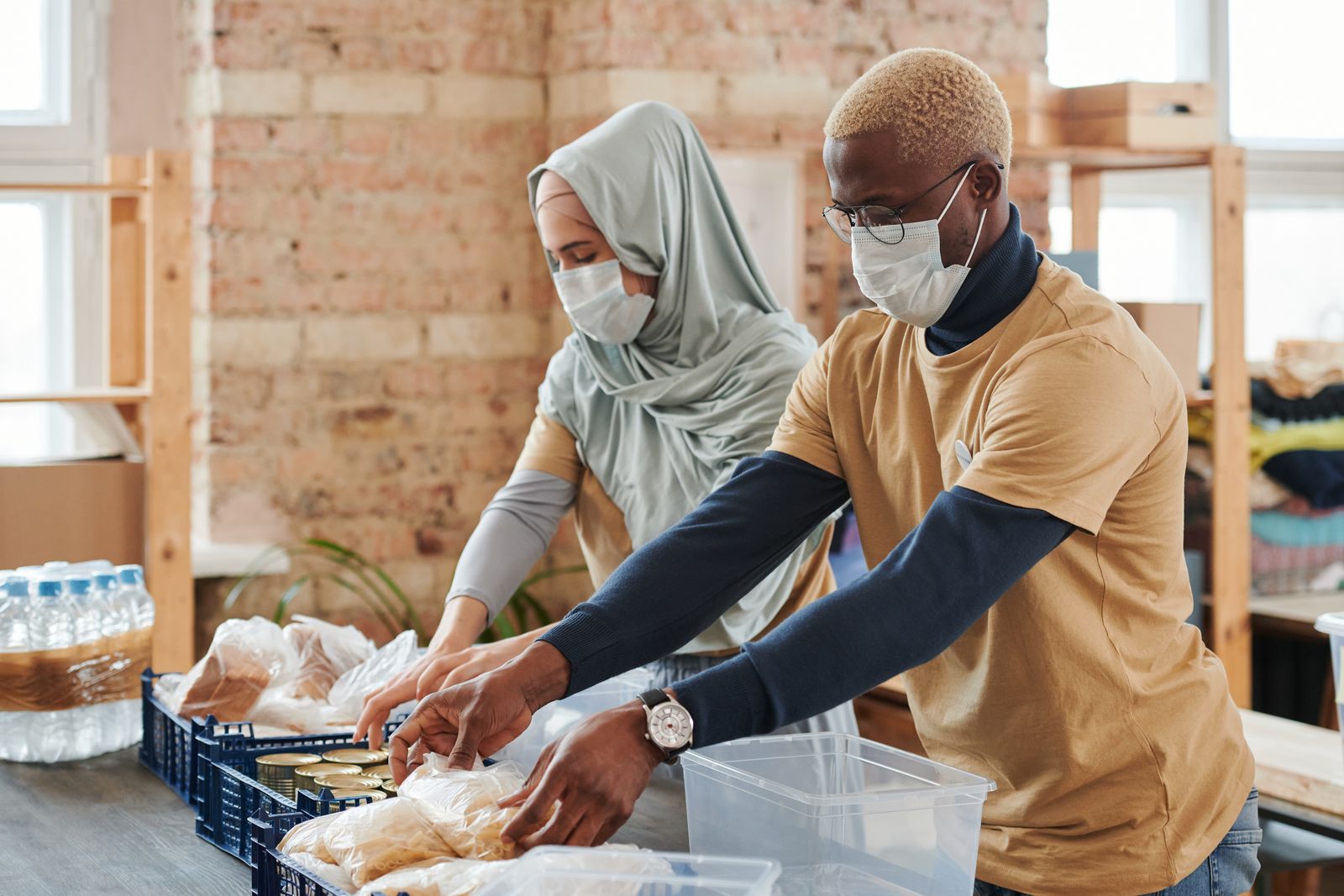 Volunteers in masks sorting food into containers on a long table