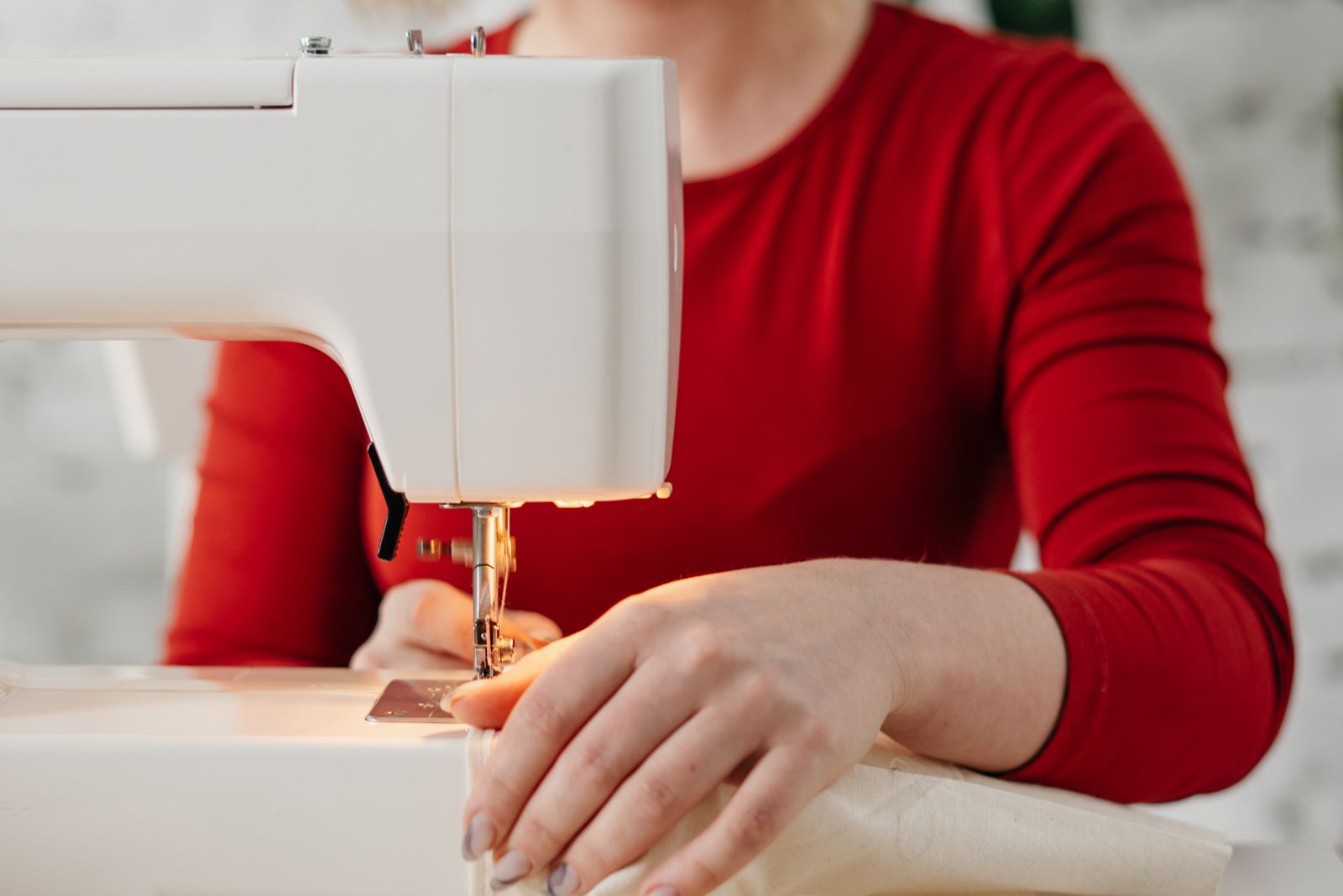 A person in a red top guiding fabric through a sewing machine